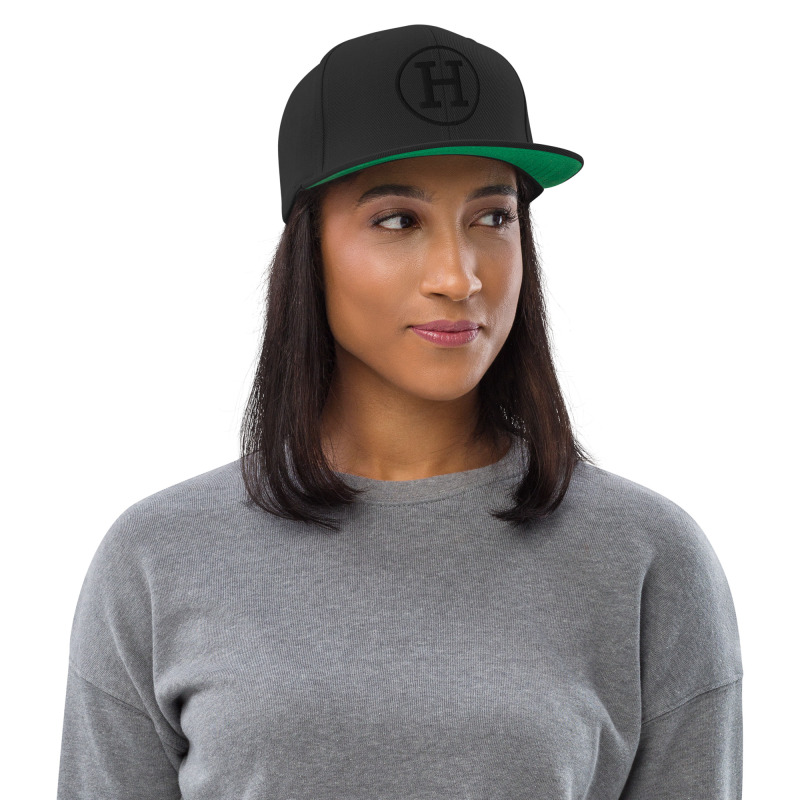 A young woman wearing a black snapback hat with the logo for certified-haters.com embroidered on the front of the hat.