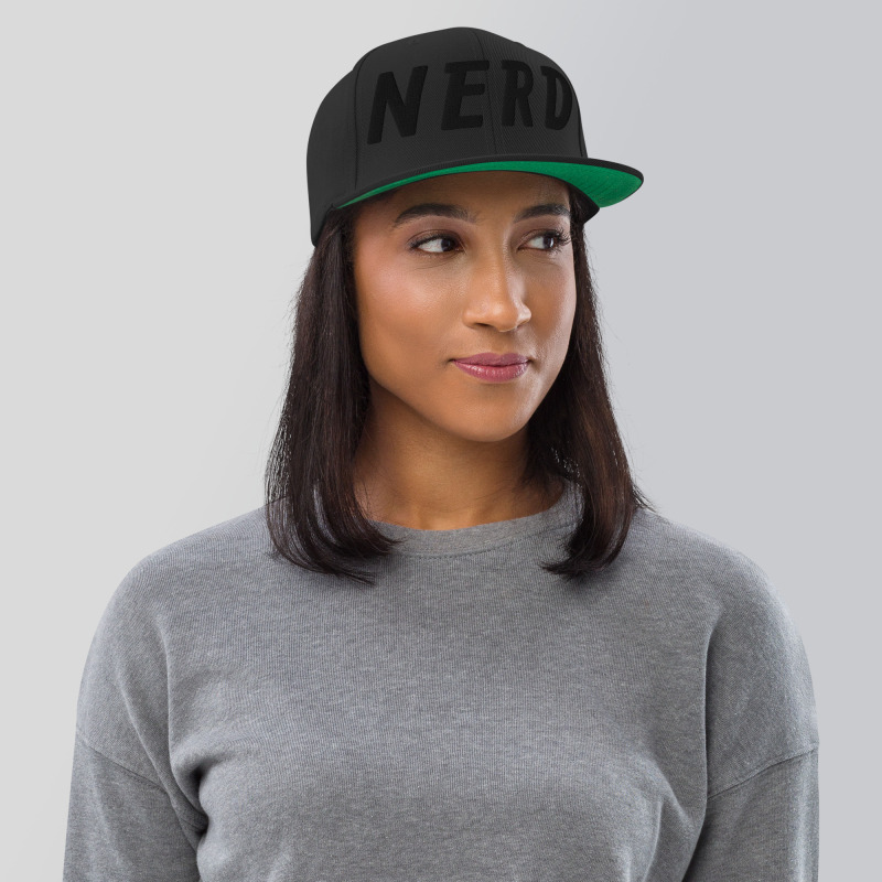 A young woman wearing a black snapback hat with the word "Nerd" embroidered in black on the front of the hat.