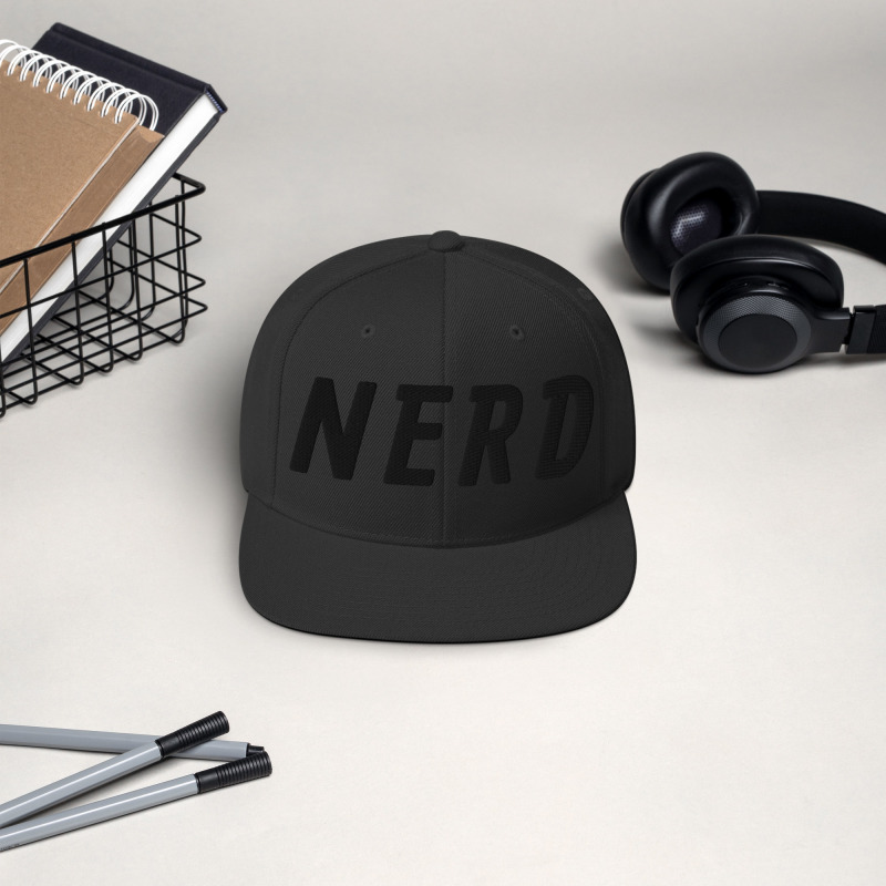 A black snapback hat with the word "Nerd" embroidered in black on the front of the hat.