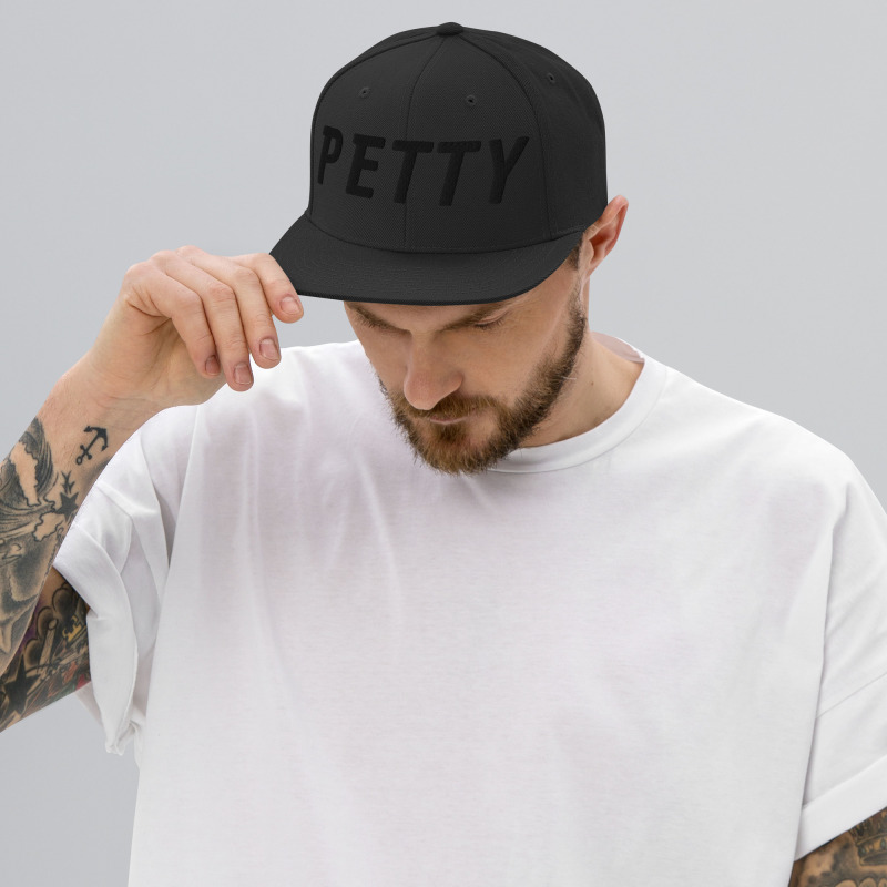 A young man wearing a black snapback hat with the word "Petty" embroidered in black on the front of the hat.