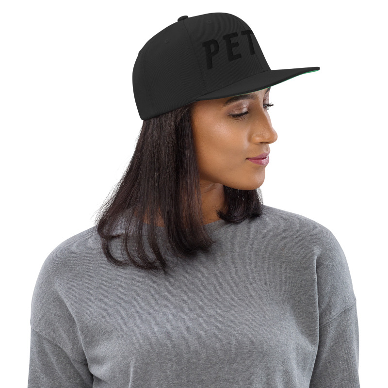 A young woman wearing a black snapback hat with the word "Petty" embroidered in black on the front of the hat.