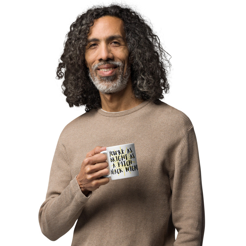 A man holding a funny mug that says "You're as bright as a pitch black night".
